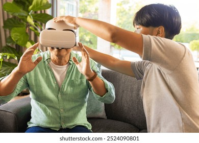 Using VR headset, asian father experiencing virtual reality with assistance in living room. Technology, immersive, indoors, interaction - Powered by Shutterstock