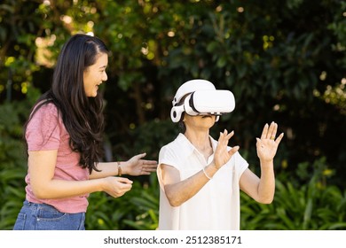 Using VR headset, asian grandmother exploring virtual reality with daughter outdoors. Technology, family, senior, bonding - Powered by Shutterstock