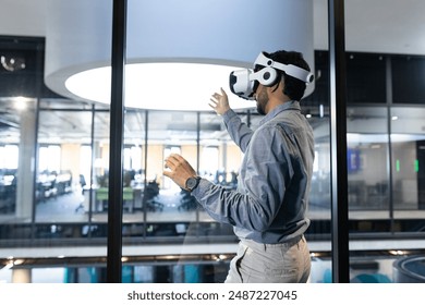 Using VR headset, man interacting with virtual environment in modern office, copy space. Technology, virtual reality, innovation, interaction, immersive, digital