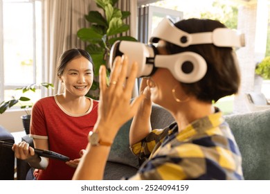 Using VR headset, mother interacting while girl with tablet smiling nearby. Virtual reality, technology, interaction, family, bonding, happiness - Powered by Shutterstock