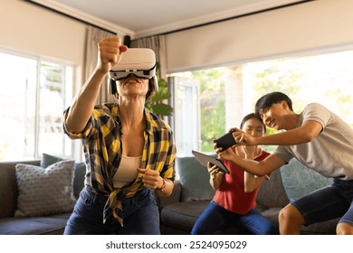 Using VR headset, mother playing game while family members watching and laughing. gaming, laughter, entertainment, technology, fun, interaction - Powered by Shutterstock