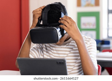 Using VR headset, student exploring virtual reality with tablet in school classroom. Technology, virtual learning, education, immersive, innovation, digital