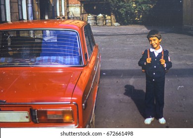 USSR, LENINGRAD - CIRCA 1982: Vintage photo of little first grader with backpack in his yard at red family soviet Lada car