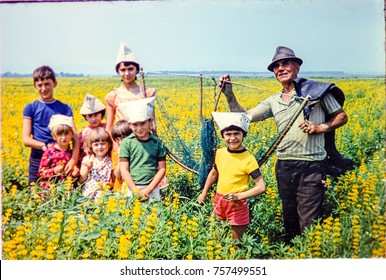 USSR, WESTERN UKRAINE, DOLISHNEE VILLAGE - CIRCA 1983: Vintage Photo Of Soviet People Circa 1980s: Group Of Kids With Adult Man On Meadow Yellow Flowers Landscape, Ukraine, Soviet Union