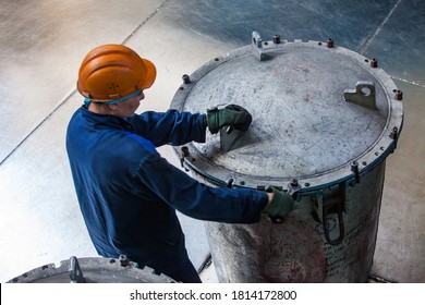 Ust'-Kamenogorsk, Kazakhstan - May 31, 2012: Worker In Blue Work Wear And Orange Hardhat. Grey Scratched Metal Bin With Metal Titanium Sponge. Raw Material For Clear Titanium.