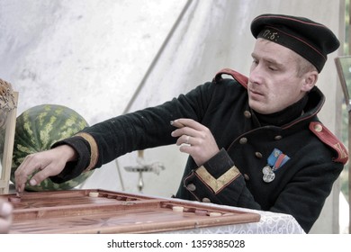 Ustyuzhna, Vologda Region, September 14, 2013. Speech Club Historical Reconstruction. A Man Dressed In Uniforms From The Time Of The Napoleonic Wars Plays Backgammon And Smokes A Cigar.