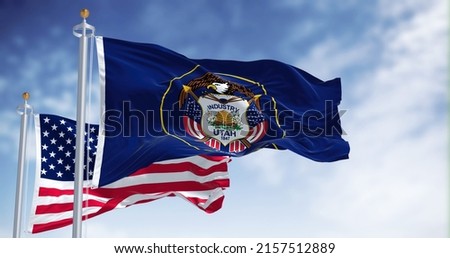 The Utah state flag waving along with the national flag of the United States of America. Utah is a state in the Mountain West subregion of the Western United States