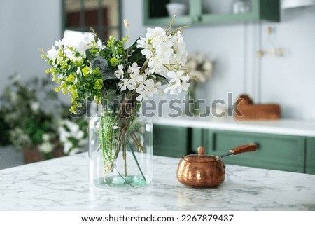 Utensil on dining table. Summer white flowers in vase and turk with coffee in kitchen table. Bouquet of flowers and plants in glass vase at home. Home interior with cozy Scandinavian decor. 