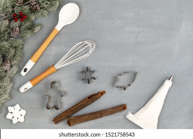 Utensils For Christmas Cooking Or Baking With Spoon, Whisk, Cookie Cutter, Icing Piping Bag, Cinnamon Sticks And Snow Flake, With Fir Branch Over Stone Like Background