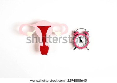 Uterus symbol with alarm clock on white background. Women's health, feminine age, menopause, climacteric, menstrual periods, fertility concept.