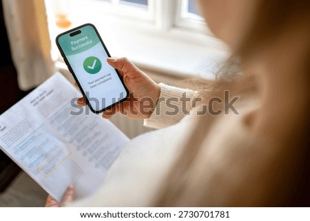 Utility bills successfully paid using mobile banking app on smartphone while holding paper invoice at home. Household expenses and digital payment concept. 