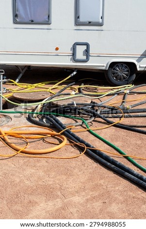 Utility hoses and heavy cables spread across the ground beneath a caravan near open service covers in a temporary hookup area for mobile accommodation.