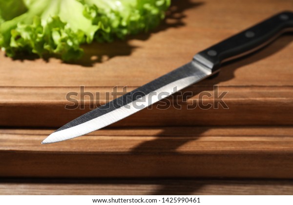 Utility knife and fresh lettuce leaves on wooden\
table, closeup. Clean\
dishes