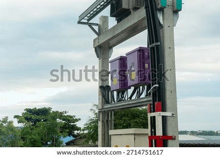 A utility pole with purple control boxes stands by a body of water, showcasing essential electrical infrastructure in a modern urban environment.