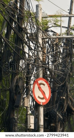 Utility pole with tangled electrical cables and no parking sign.