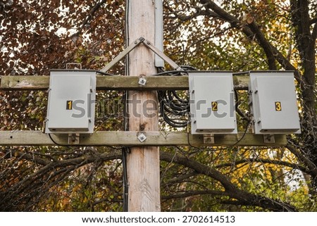 Utility pole with three numbered electrical junction boxes mounted on wooden beams, surrounded by autumn foliage in an outdoor infrastructure setting. High quality photo
