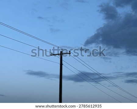 Utility power pole and electrical lines against evening sky with clouds creating infrastructure and energy transmission concept