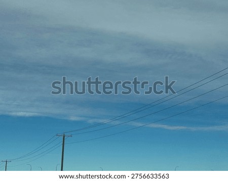 Utility power pole with overhead electrical lines against blue sky with cloud patterns