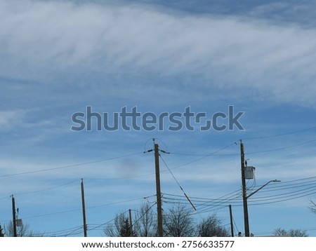 Utility power pole with overhead electrical lines against blue sky with cloud patterns