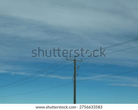 Utility power pole with overhead electrical lines against blue sky with cloud patterns