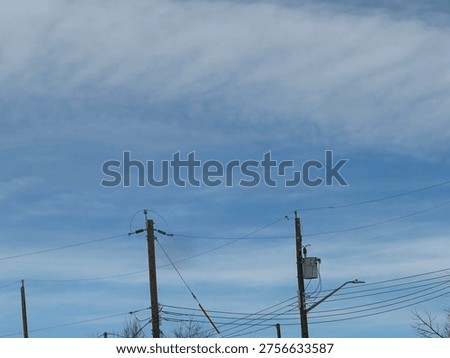Utility power pole with overhead electrical lines against blue sky with cloud patterns
