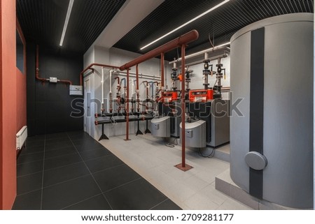 The utility room features a modern heating system with neatly arranged pipes, boilers, and control panels. The space is well-lit, showcasing the efficient design of the installation.