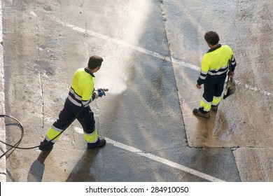 Utility Service Company Men Workers Cleaning The Street  With Water Pressure At City