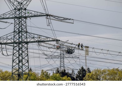 Utility technicians performing maintenance work on high voltage transmission lines suspended between large electricity pylons, power grid infrastructure, electrical engineering and energy distribution