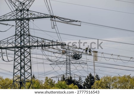 Utility technicians performing maintenance work on high voltage transmission lines suspended between large electricity pylons, power grid infrastructure, electrical engineering and energy distribution