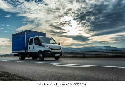 Utility Transportation Van Or Mini Truck Driving Through Highway With Dramatic Sunset Sky In The Background. Transportation Vehicle