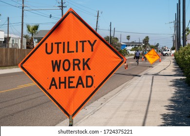 Utility Work Ahead Sign On Sidewalk Next To Street Warns Traffic About Work Project Zone In Distance.