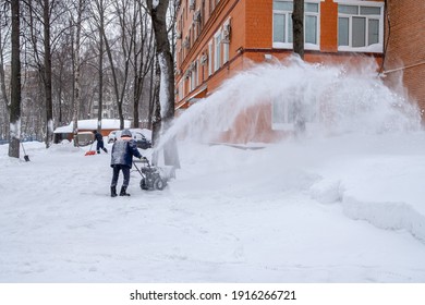 A Utility Worker Cleans A Path With A Snow Blower During Heavy Snow On A Winter Day. A Jet Of Snow Takes Off Into The Air.