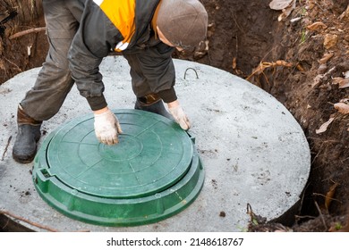 A Utility Worker Lifts A Manhole Cover For Sewerage Maintenance And Pumping Out Feces. Septic On A Residential Lot.