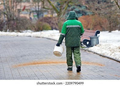 Utility Worker Sprinkle Grit And Deicing Mixture On Paving Slabs. Worker Spread Sand And Salt Mixture To Slipper Road. Road Treatment With De-icing Mixture, Melt Snow And Ice And Prevent Slipping