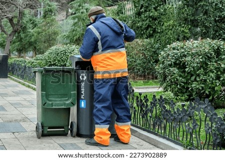 A utility worker in uniform removes garbage from a bin on a city street.