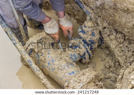 Utility worker using tool to repair the broken pipe valve for commercial building water supplies. Utility worker fixing broken water main.