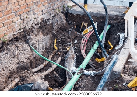 Utility workers are excavating and working on underground utility lines.  The image shows a trench dug in the ground, revealing various types of pipes and cables