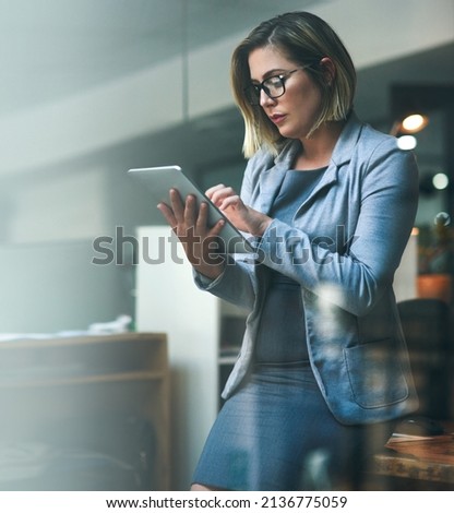 Utilizing smart tools to beat the deadline. Shot of a young businesswoman working late on a digital tablet in an office.