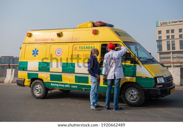 Uttar Pradesh, India, 17 February 2021: Man\
assisting Ambulance Car Moving With Siren Emergency Ambulance\
Reanimation Van Car On\
Street.
