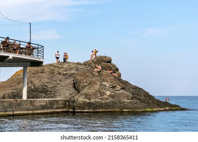 Utyos( Utes), Alushta, Crimea - September 15, 2021: People on the sea rock sunbathe and swim. In the foreground - a cafe hanging over the sea with visitors