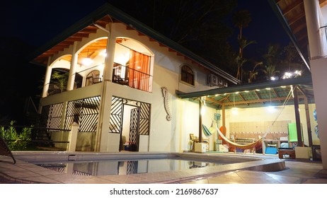 Uvita, Costa Rica-March 2018: Spectacular Outdoor Scenery Of Real Estate Property In Jungle Environment With A Swimming Pool During The Nighttime With Colourful Decorative Lights Turned On. 