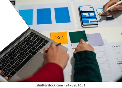 UX developer and ui designer brainstorming about mobile app interface wireframe design with customer breif and color code at office.