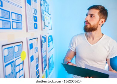 Ux Graphic Designer Man Develops The Idea Of User Interaction In A Web Application. Design Of Mobile Applications. A Man Is Studying A Concept Plan. Graphic Designer At Work.