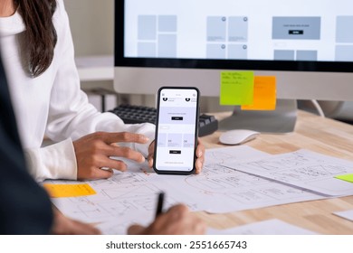 UX UI designer testing prototype on a phone, discussing and brainstorming on wireframes for a website and mobile app prototype, in the concept of website and mobile application design concept.