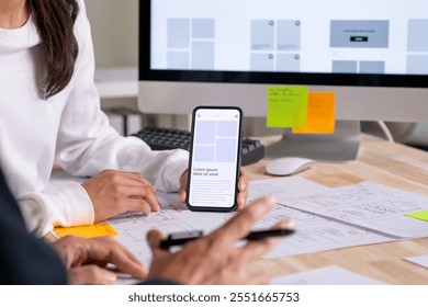 UX UI designer testing prototype on a phone, discussing and brainstorming on wireframes for a website and mobile app prototype, in the concept of website and mobile application design concept.
