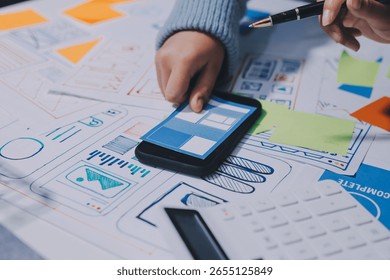 UX UI designer testing prototype on a phone, discussing and brainstorming on wireframes for a website and mobile app prototype, in the concept of website and mobile application design concept.