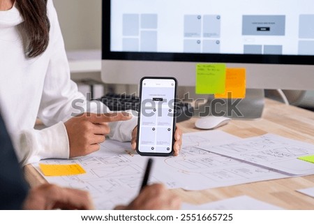 UX UI designer testing prototype on a phone, discussing and brainstorming on wireframes for a website and mobile app prototype, in the concept of website and mobile application design concept.