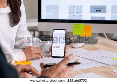 UX UI designer testing prototype on a phone, discussing and brainstorming on wireframes for a website and mobile app prototype, in the concept of website and mobile application design concept.