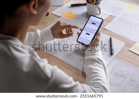 UX UI designer testing prototype on a phone, discussing and brainstorming on wireframes for a website and mobile app prototype, in the concept of website and mobile application design concept.