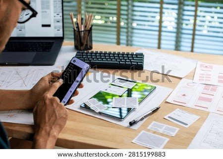 UX UI designer testing prototype on a phone, working on wireframes for a website and mobile app prototype, in concept of website and mobile application design concept.